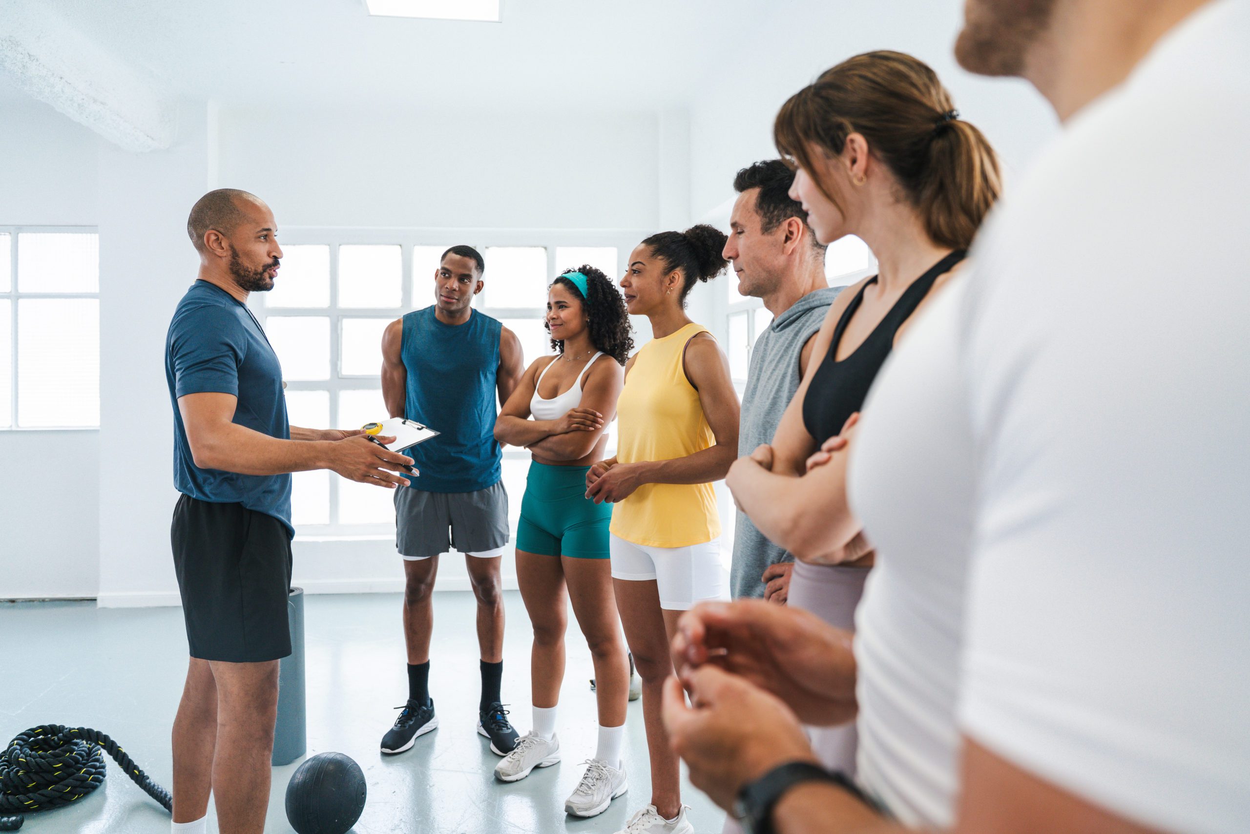 Multiethnic group of sportive people doing functional workout in training class gym personal trainer holding clipboard guiding diverse athletes through functional training in bright gym setting
